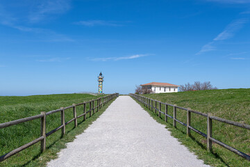 Fototapeta premium Colorful lighthouse guiding visitors along a gravel path in bareyo, cantabria, spain faro de ajo punta del caballo