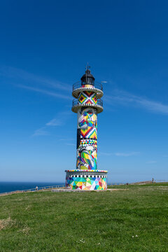 Ajo lighthouse stands on a green cliff, showcasing vibrant abstract art against a blue sky faro de ajo punta del caballo
