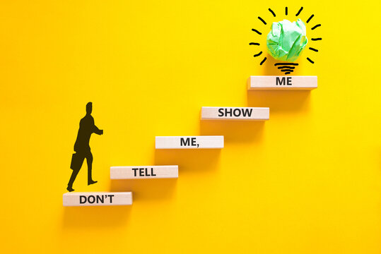 Tell or show symbol. Concept words Do not tell me, show me on beautiful wooden blocks. Beautiful yellow paper background. Light bulb icon. Businessman icon. Business tell or show concept. Copy space.
