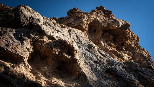 Volcanic rock formation with porous texture under clear blue sky. Natural erosion patterns ideal for geology background and nature texture use