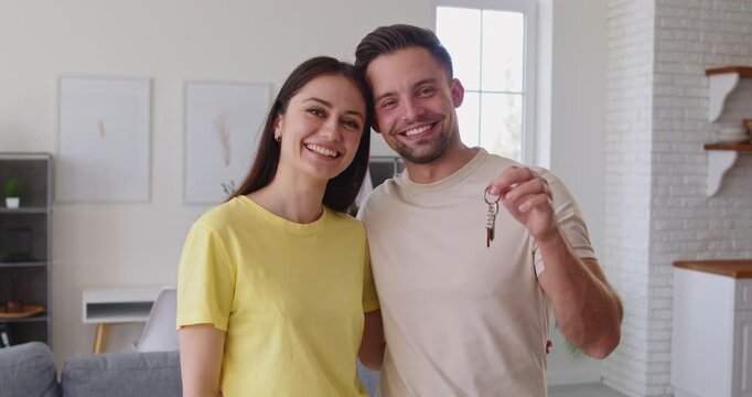 Happy family couple holding keys from their new house, glad to become houseowners, embracing and smiling happily, going to start new life in spacious apartment. Rental and moving concept