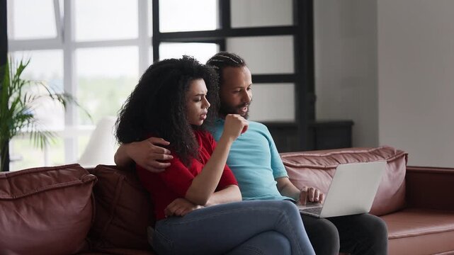 Happy African American couple shopping online on laptop, booking cinema tickets