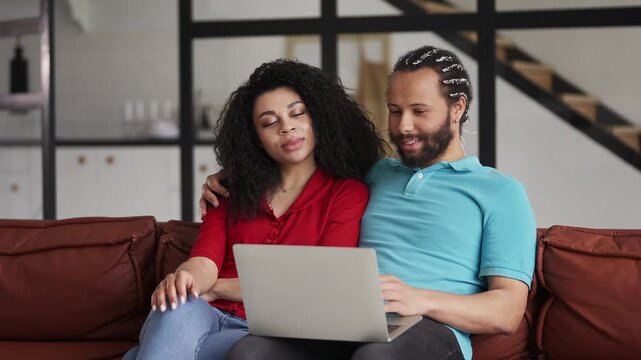 Smiling Black couple choosing a vacation tour on a laptop, shopping at home