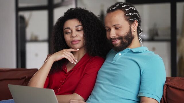 Young African American couple shopping online on a laptop on couch at home