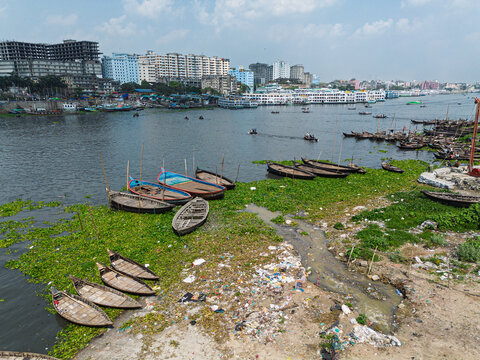 Aerial view of Buriganga River with wooden boats moored near the shore and the city skyline in Dhaka, Dhaka Division, Bangladesh.