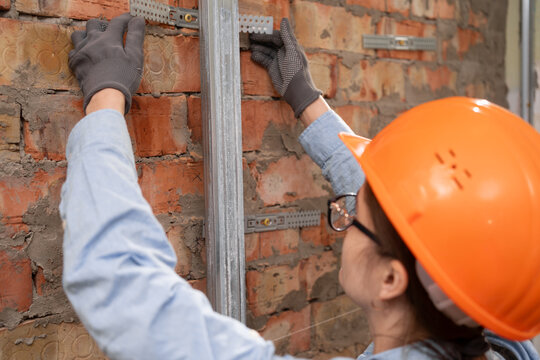 Close-up of woman in helmet fixing metal drywall frame using suspension hanger. Interior construction in new building.