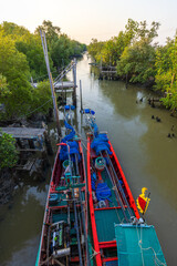 Fototapeta premium Traditional Thai long-tail fishing boats moored in a mangrove forest canal at sunset,High-angle view of two colorful wooden fishing boats docked along a narrow tidal canal surrounded by lush mangrove 