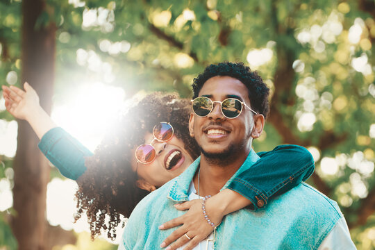 Young couple smiling and having fun outdoors in a sunny park, wearing sunglasses and denim jackets, expressing joy and love together