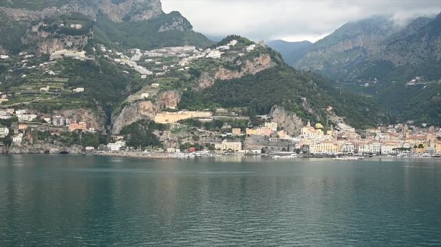 Scenic 3K view from the Mediterranean Sea toward the dramatic Amalfi Coast in southern Italy, featuring colorful hillside villages, rugged mountains and calm coastal water.