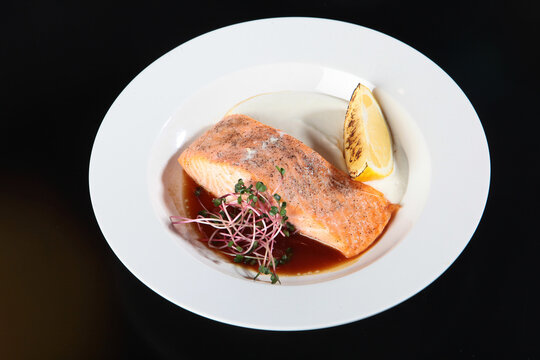 Grilled salmon fillet with lemon slice. Grilled lemon slice. A piece of salmon on a white plate, garnished with microgreens and spices. Healthy and delicious food.