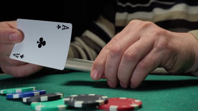 Hands of a person shuffling a deck of playing cards while placing poker chips on a green felt table in a dimly lit gaming environment