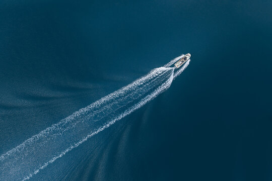 Aerial view of a small white boat cruising across deep blue sea water leaving a long white foamy wake in Itoshima, Fukuoka, Japan.