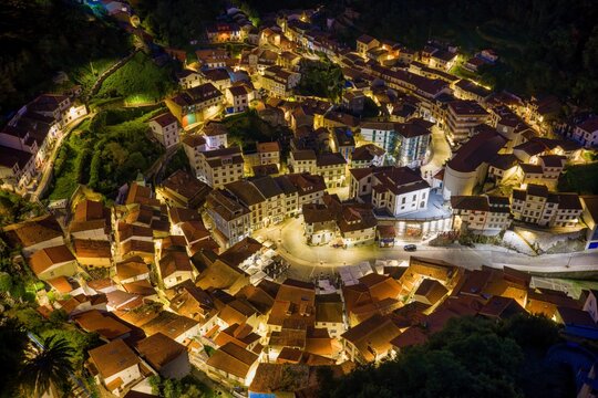 Aerial view of the illuminated historic town of Cudillero at night with its characteristic red-tiled rooftops and glowing streets nestled in the hills Cudillero, Asturias, Spain.