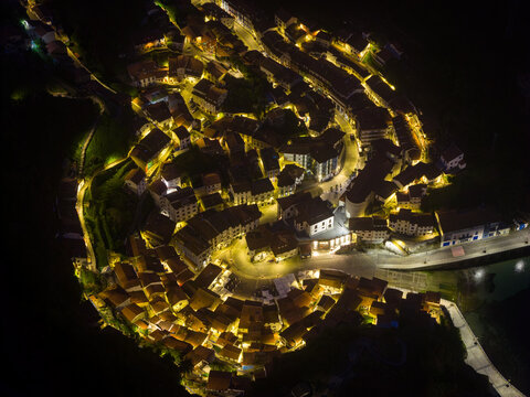 Aerial view of the illuminated coastal town of Cudillero at night with warm streetlights highlighting the traditional houses and central plaza Cudillero, Asturias, Spain.