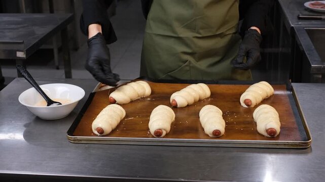 Male chef in professional restaurant kitchen sprinkling sesame seeds on buns before baking

