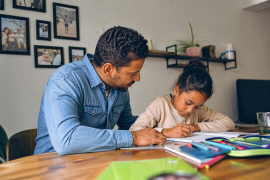 Vater unterst&uuml;tzt seine Tochter bei den Hausaufgaben am Tisch, konzentriertes Lernen in gem&uuml;tlicher Wohnatmosph&auml;re, Bildung und Familienzeit im Alltag.