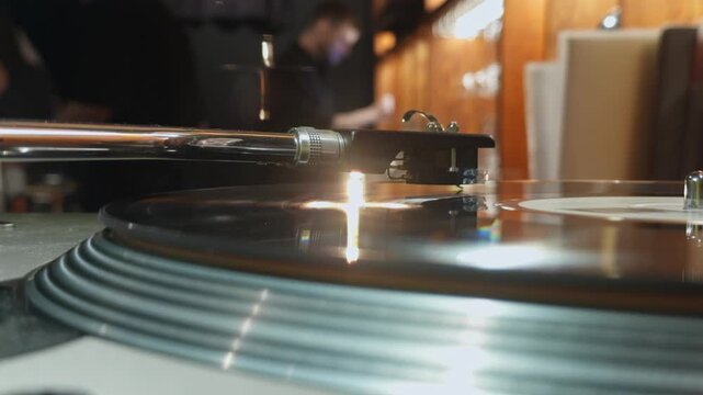 close-up of a vinyl record player with a rotating vinyl record, a tonearm with a pickup needle, DJ hands changing the record, remote control, bar