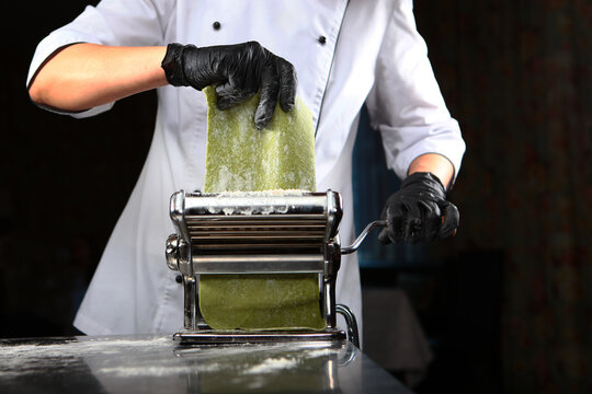 Machine for making pasta and rolling out dough. Cooking pasta with spinach. Chef prepares the dough with spinach. Spinach is natural dye for dough in green color.