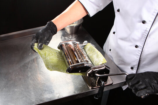 Chef prepares the dough with spinach. Machine for making pasta and rolling out dough. Spinach is natural dye for dough in green color. Cooking pasta with spinach.