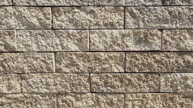 A textured stone wall featuring rectangular blocks in shades of beige and light brown, arranged in a staggered running bond pattern with visible mortar lines.