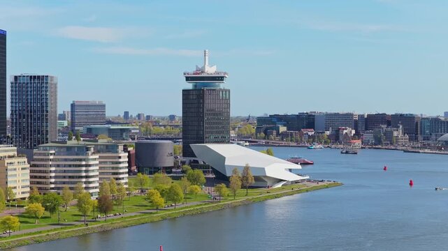 Amsterdam cityscape capturing ADAM Toren and EYE Film Museum along IJ river waterfront with boats sailing on tranquil water under clear sky on sunny day in Netherlands