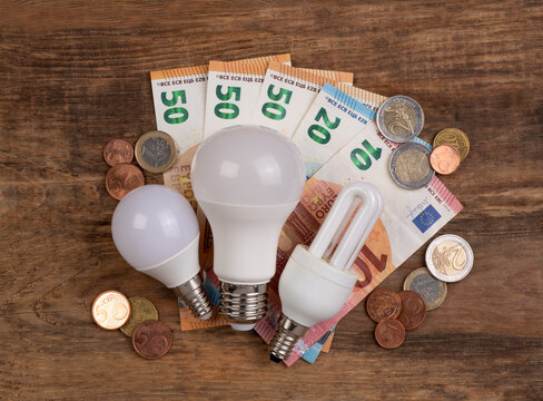 Cost of electricity concept. Light bulbs and money on a wooden background, top view.