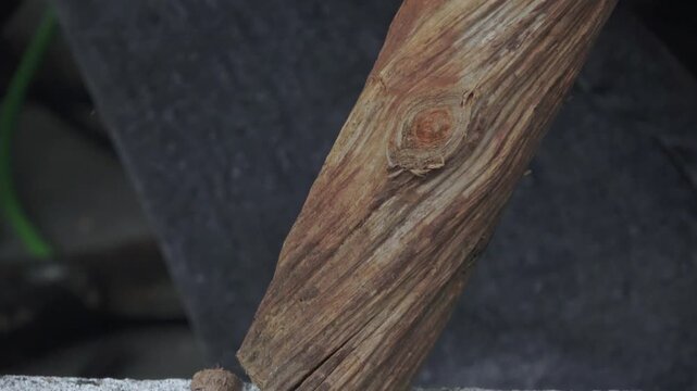 A high-quality, handheld close-up shot capturing the traditional process of woodworking. The footage shows a craftsman meticulously shaving the edges of a small wooden branch using a sharp large mache