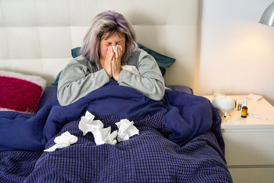 Woman blowing nose in bed having a cold