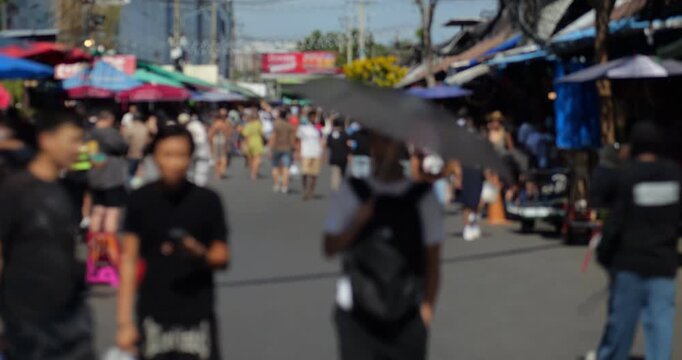 Rapid motion of people in daytime time-lapse shot with defocused view. Tourists walk around Chatuchak weekend market in hot sunny day. Due to accelerated effect this shopping area looks crowded