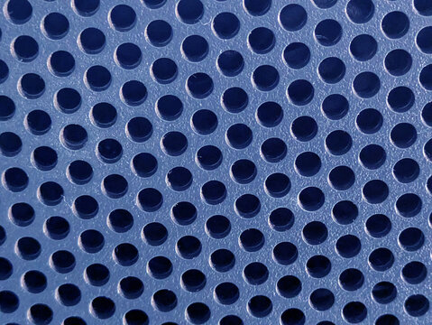 Close-up of shiny perforated metal surface with blurred background and patterned holes