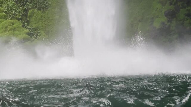 Crashing waterfall creates turbulent white foam and thick mist over churning emerald waters in dramatic closeup creating powerful natural force