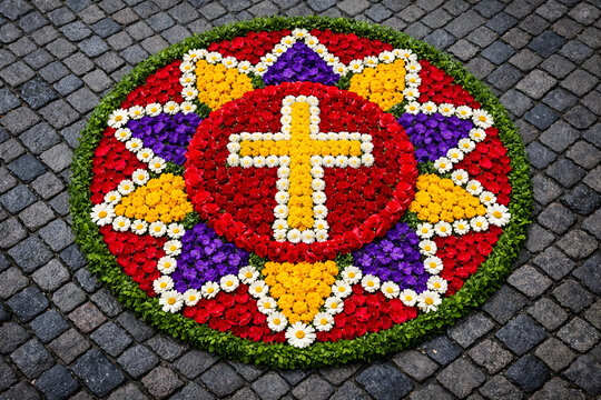 round floral mandala with cross made of petals on cobblestone, corpus christi procession decoration, colorful fronleichnam street art