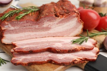 Fototapeta premium Pieces of smoked bacon, rosemary and tomatoes on light grey wooden table, closeup