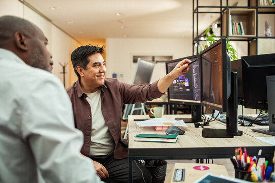 Two coworkers collaborating on dual monitors in modern office