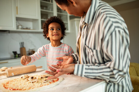 Parent and child making pizza together in a home kitchen