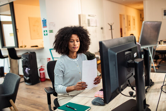 Focused professional reviewing documents at computer in modern office