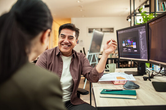 Smiling designer collaborating with coworker at dual monitors in modern office