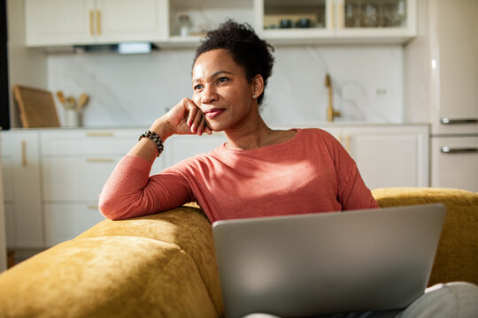 Thoughtful woman with laptop on sofa at home