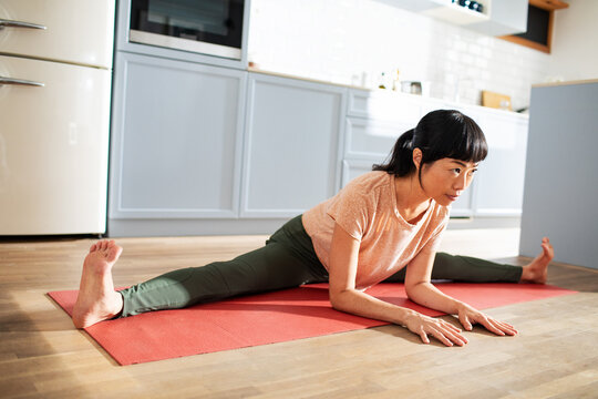 Woman practicing yoga splits on a mat in home kitchen