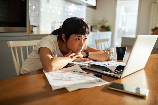Woman stressed over household bills at laptop in home kitchen