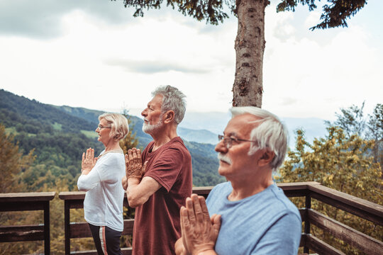 Senior friends meditating with prayer hands on mountain deck