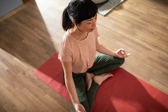 Woman meditating on red yoga mat at home