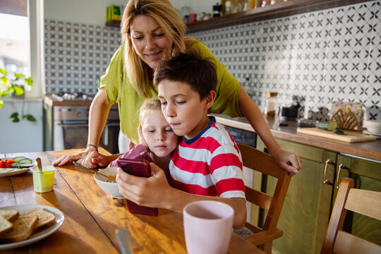 Mother with two children using smartphone at kitchen table