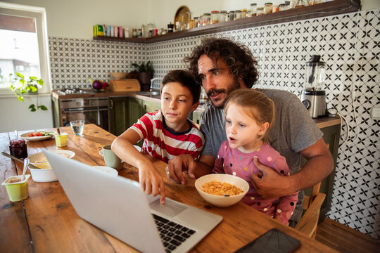 Father and kids using laptop at home kitchen table
