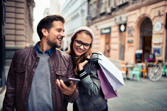 Happy couple shopping with smartphone on city street