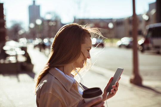 Young woman with coffee using smartphone on city street