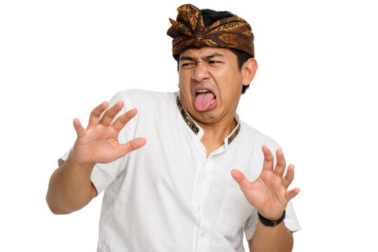 Disgusted Balinese man in traditional udeng headwear, expressive male sticking out tongue with repulsed face, man showing aversion and dislike