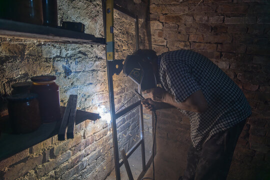 Man welding metal frame in dimly lit workshop