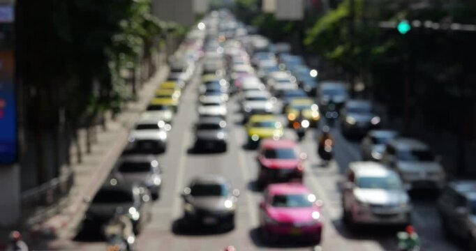 Defocused lengthwise perspective of heavy traffic on city road in Bangkok on sunny day. Roadway is densely packed with many vehicles that begin to move forward as signal changes.