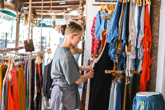 Young woman choosing clothes in thrift-style boutique, conscious shopping, slow fashion, circular fashion, sustainable wardrobe and responsible consumption concept.